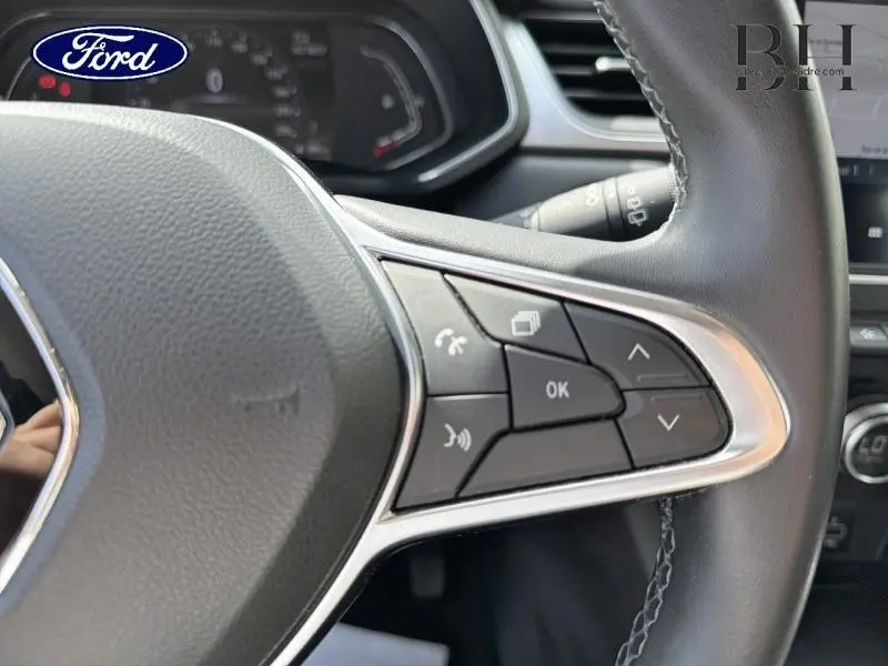 Gros plan sur les commandes au volant noir et chrome d'un Renault Captur Gris Cassiopée, tableau de bord en arrière-plan.