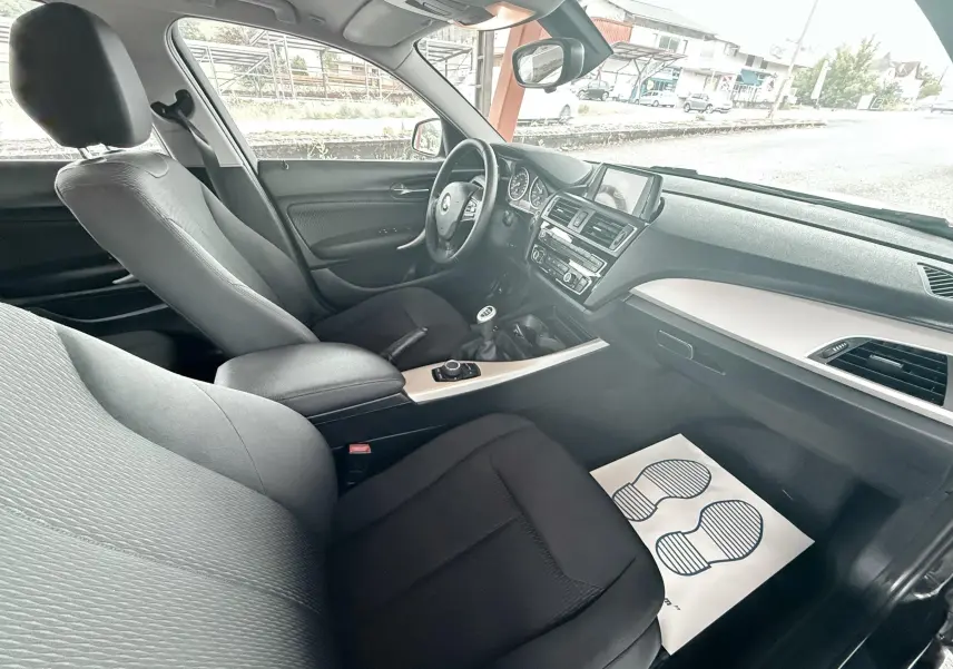 Vue intérieure côté passager avant de la BMW Série 1 noire, montrant sièges tissu noirs et tableau de bord moderne.