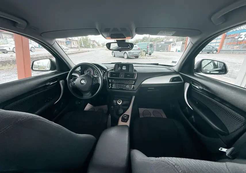 Intérieur noir de BMW Série 1 2016, vue avant centrée sur tableau de bord et volant avec boîte manuelle.