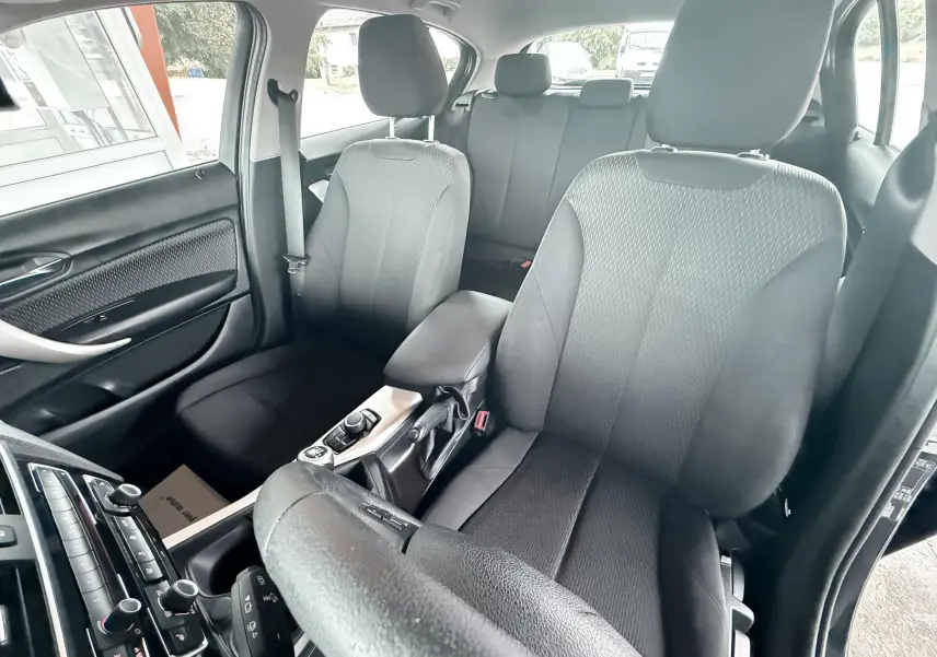 Vue intérieure de la BMW Série 1 2016 montrant les sièges avant en tissu noir et la console centrale.
