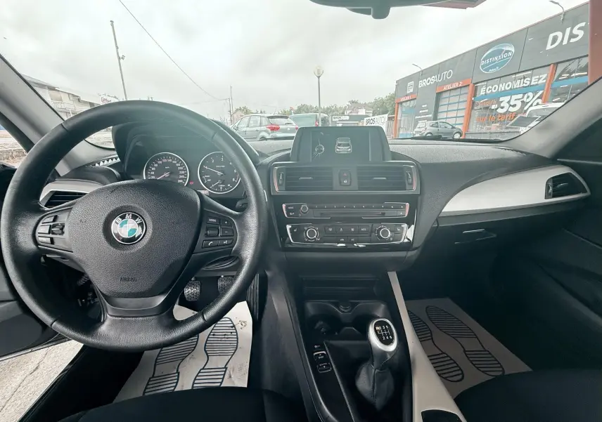 Intérieur noir de BMW Série 1 2016, vue du poste de conduite avec volant, tableau de bord et levier de vitesses manuel.