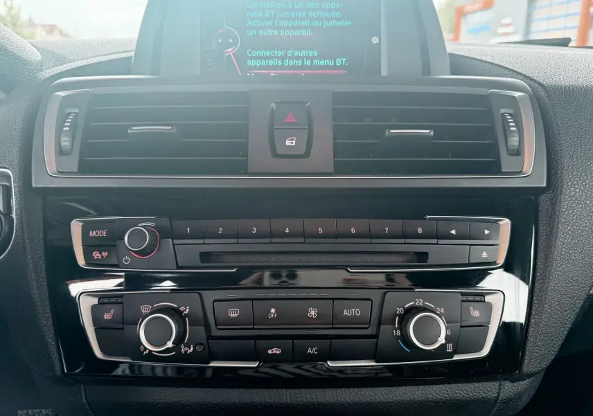 Vue rapprochée du tableau de bord central de la BMW Série 1 noire, montrant la console multimédia et les commandes de climatisation.