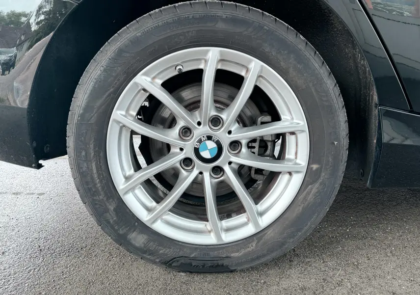 Gros plan sur la roue avant droite d’une BMW Série 1 noire, mettant en valeur la jante alliage argentée et le logo BMW central.