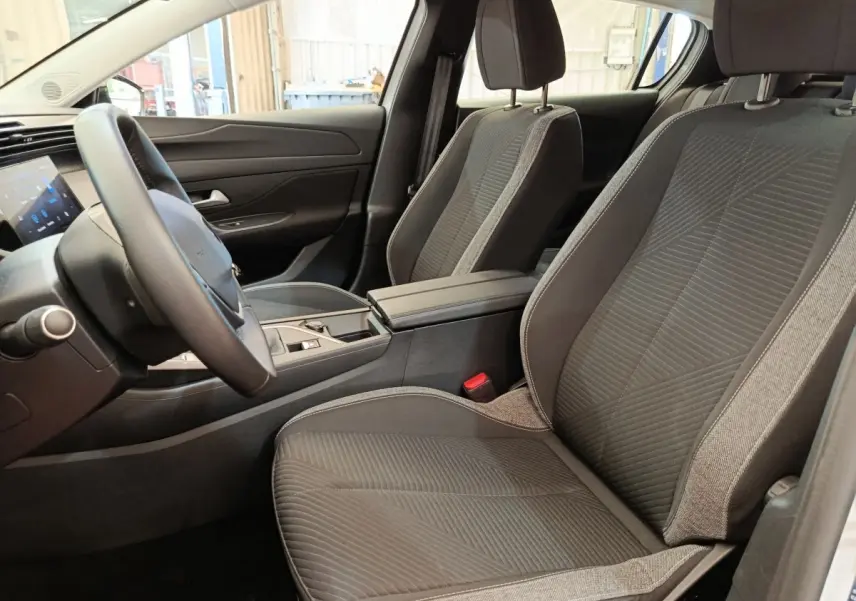 Vue intérieure côté conducteur de la Peugeot 308 2024 avec sièges tissu gris et volant cuir multifonctions.