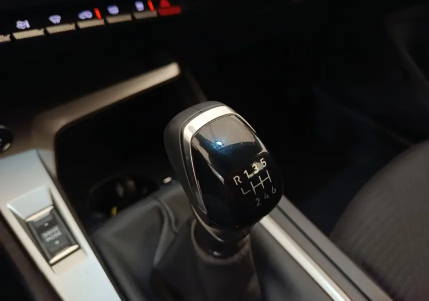 Gros plan sur le levier de vitesses manuel noir de la Peugeot 308 2024, intérieur avec console argentée et siège tissu gris.