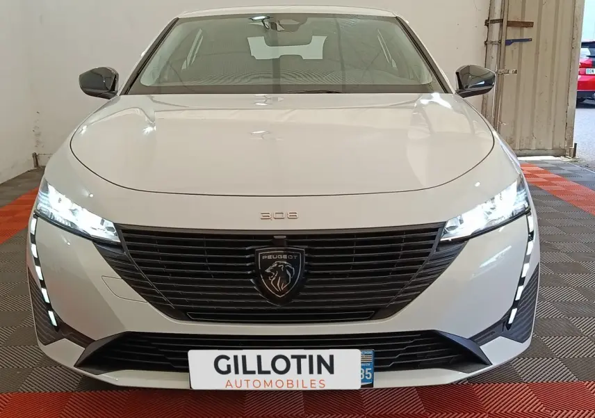 Vue frontale d'une Peugeot 308 blanche 2024 avec calandre noire et feux LED allumés en intérieur.