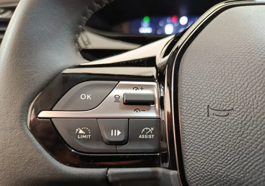 Gros plan sur les commandes gauche du volant cuir noir d’une Peugeot 308 blanche, avec boutons de régulateur et assistances.