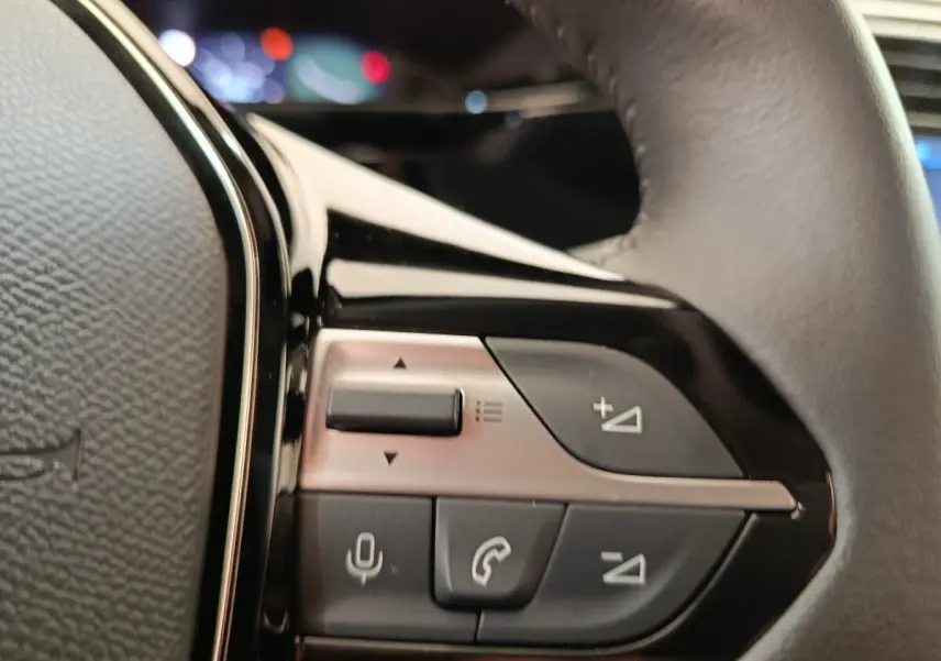 Gros plan sur les commandes multifonctions côté gauche du volant cuir d'une Peugeot 308 blanche 2024.