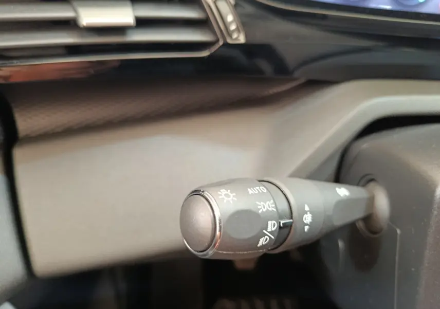 Gros plan sur la commande des phares à gauche du volant dans l'habitacle d'une Peugeot 308 blanche 2024.