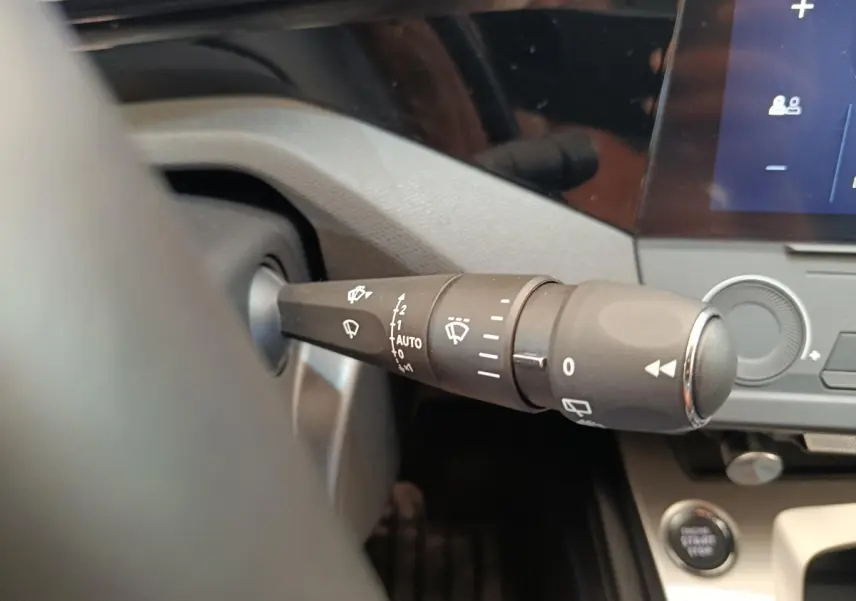 Gros plan sur la commande des essuie-glaces à gauche du volant dans l’habitacle d’une Peugeot 308 blanche 2024.