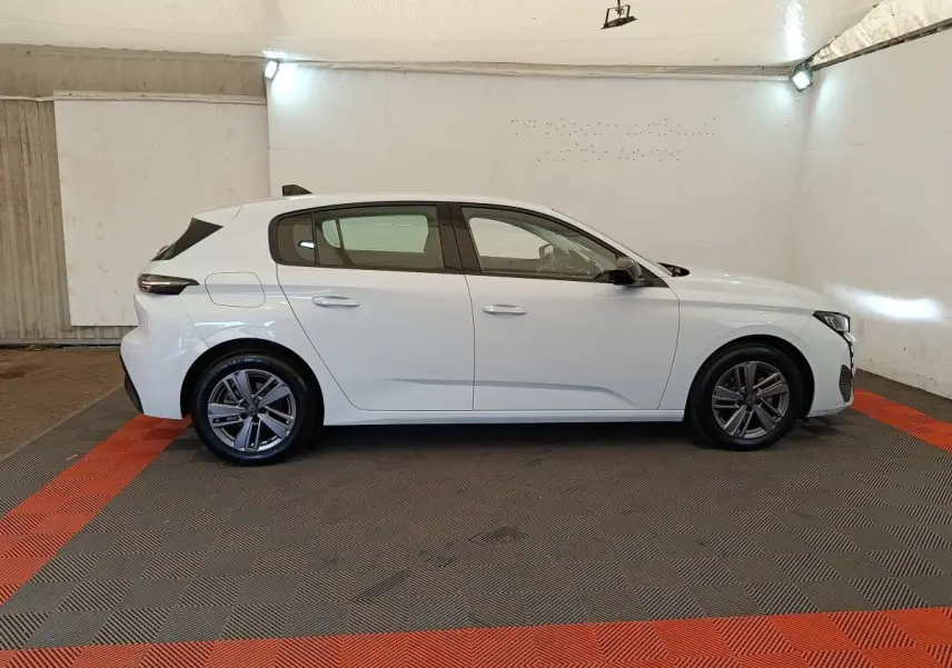 Peugeot 308 blanche vue de profil côté gauche dans un garage, avec jantes alliage et feux arrière LED distinctifs.