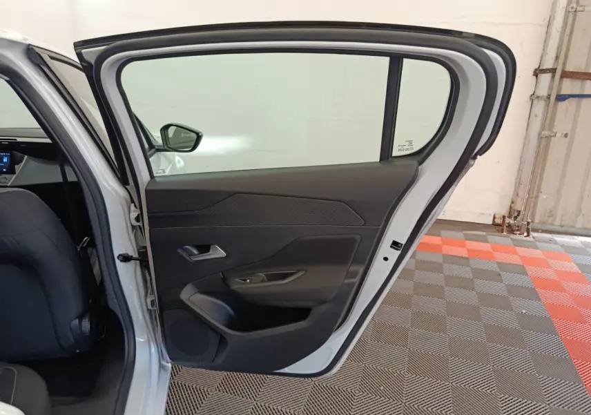 Vue intérieure de la porte arrière gauche ouverte d'une Peugeot 308 blanche, avec garniture noire et poignée intégrée.