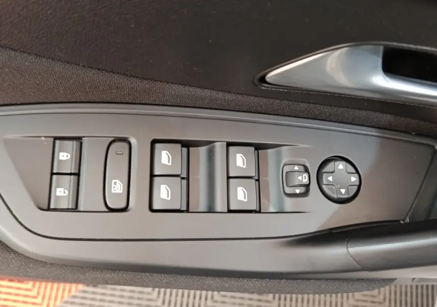 Gros plan sur les commandes de lève-vitres et rétroviseurs côté conducteur d'une Peugeot 308 blanche 2024.