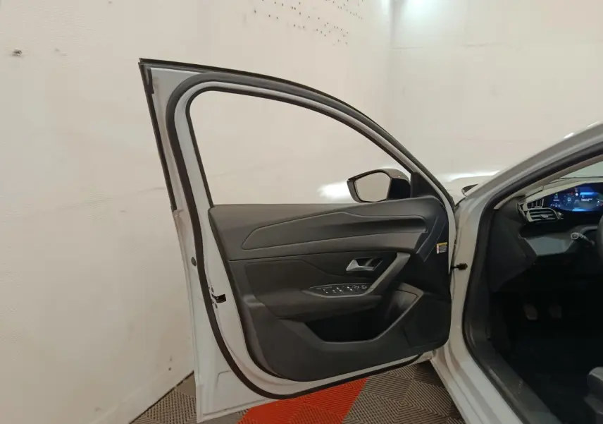 Portière avant gauche ouverte d’une Peugeot 308 blanche, montrant l’intérieur noir et les commandes de vitres.