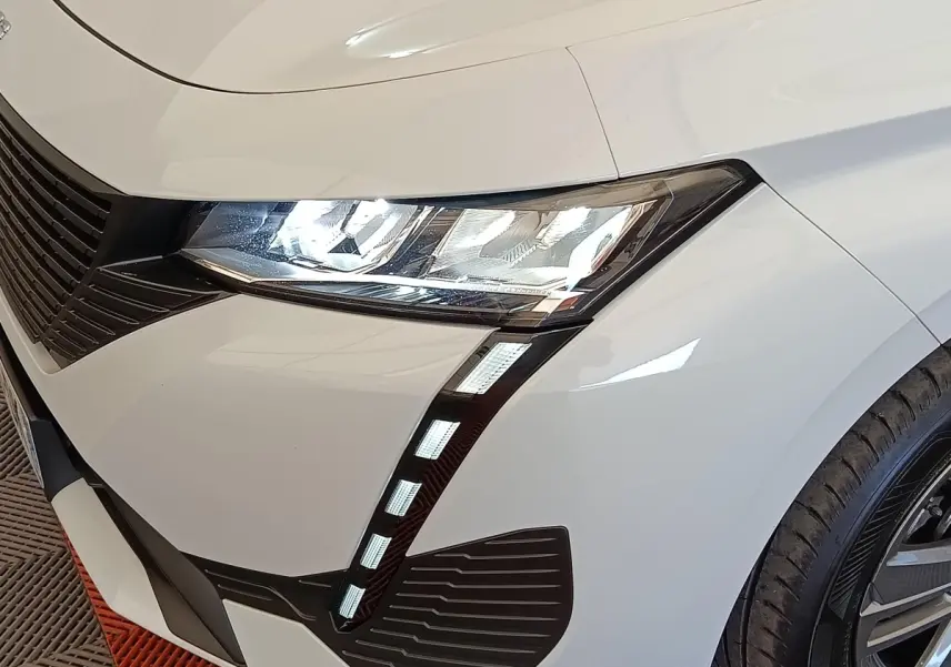Gros plan sur l'avant droit blanc d'une Peugeot 308 2024, mettant en valeur le phare LED et la calandre noire.
