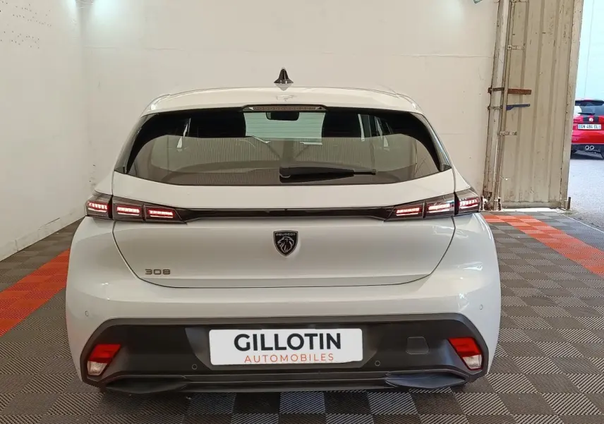 Vue arrière d'une Peugeot 308 blanche 2024 avec feux LED allumés dans un garage.
