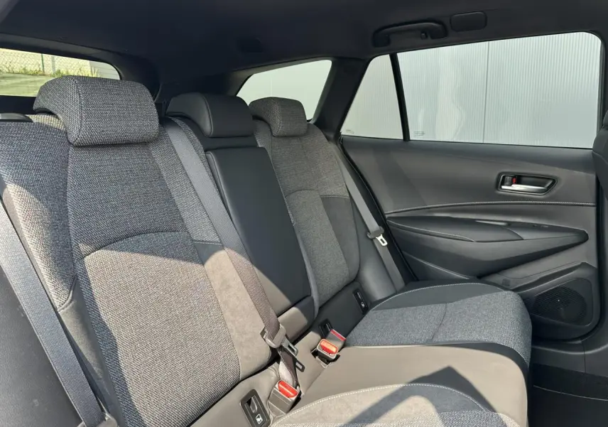 Vue intérieure côté droit des sièges arrière gris et noir de la Toyota Corolla Touring Sport 2025 avec habillage sobre et ceintures visibles.
