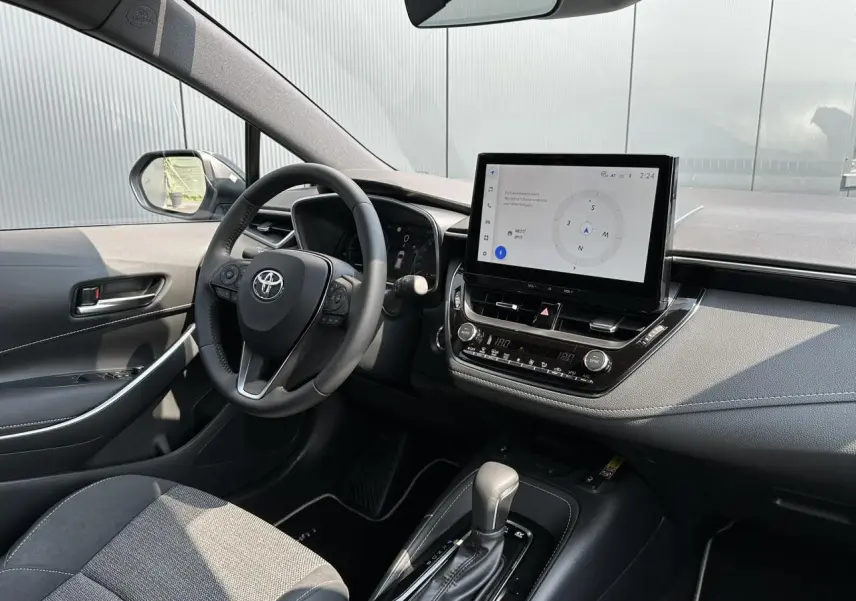 Intérieur de la Toyota Corolla Touring Sport 1.8 Hybrid 2025, vue côté conducteur, tableau de bord et écran tactile noir.