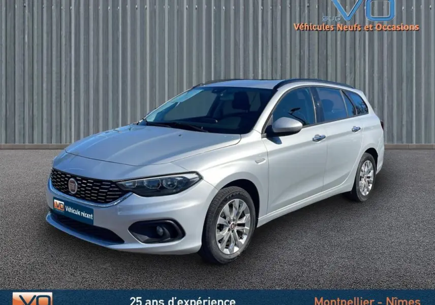 Fiat Tipo Station Wagon gris en 3/4 avant droit, avec jantes alliage et barres de toit visibles.
