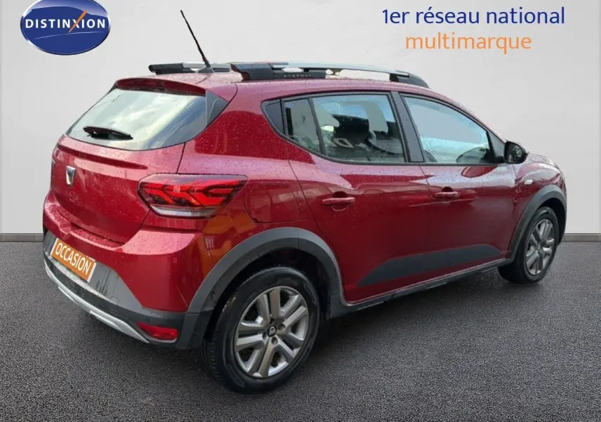 Vue 3/4 arrière droite d'une Dacia Sandero Stepway rouge fusion avec barres de toit et jantes alliage.