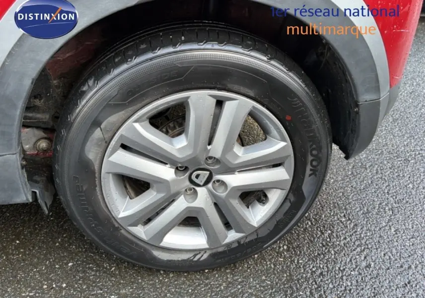 Gros plan sur la roue avant droite d'une Dacia Sandero Stepway rouge fusion, mettant en valeur la jante en alliage gris.