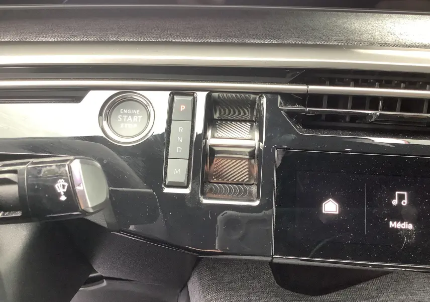 Gros plan sur la console centrale noire brillante du Peugeot 3008 Hybrid 2024, avec bouton start/stop et sélecteur de vitesse tactile.