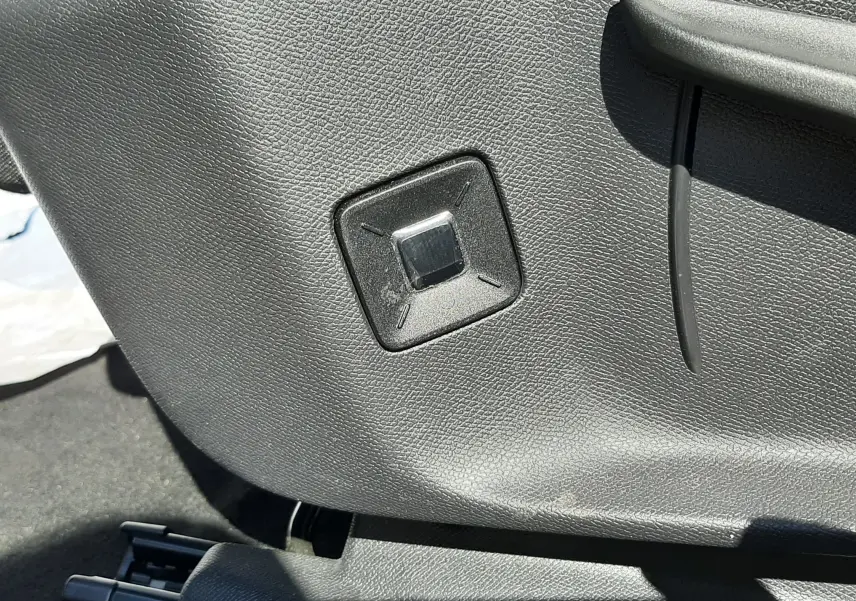 Détail du bouton de réglage électrique du siège en plastique noir à l'intérieur du Peugeot 3008 blanc Okenite.