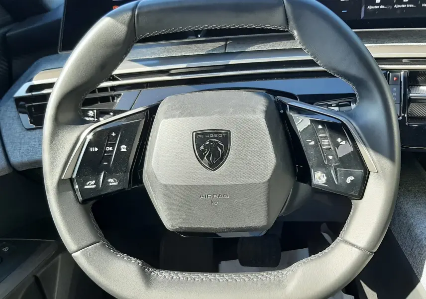 Vue rapprochée du volant cuir noir du Peugeot 3008 Hybrid 2024 avec commandes intégrées et tableau de bord numérique.