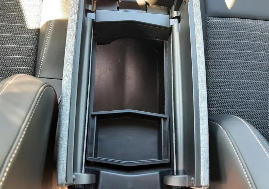 Vue plongeante sur le rangement central ouvert entre les sièges avant noirs du Peugeot 3008 Hybrid 2024.