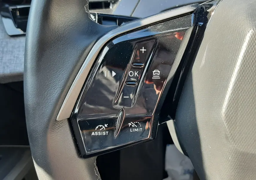 Gros plan sur les commandes noires du volant côté gauche du Peugeot 3008 Hybrid 145 blanc Okenite 2024.