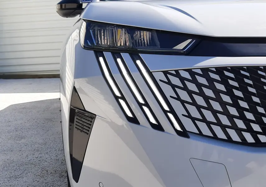Gros plan sur l'avant droit blanc Okenite du Peugeot 3008 2024 avec ses phares LED et calandre à motifs géométriques.