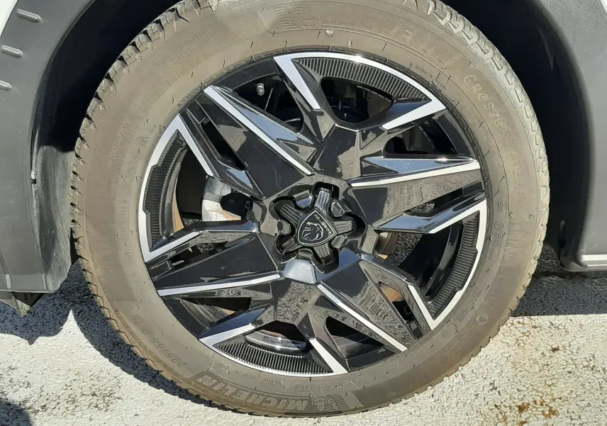 Gros plan sur la roue avant droite d’un Peugeot 3008 blanc Okenite avec jante noire et argentée au design géométrique.