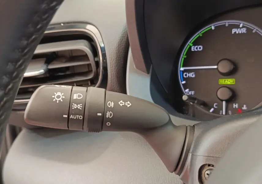 Gros plan sur la manette des phares et clignotants à gauche du volant dans l’habitacle gris clair de la Toyota Yaris hybride 2022.
