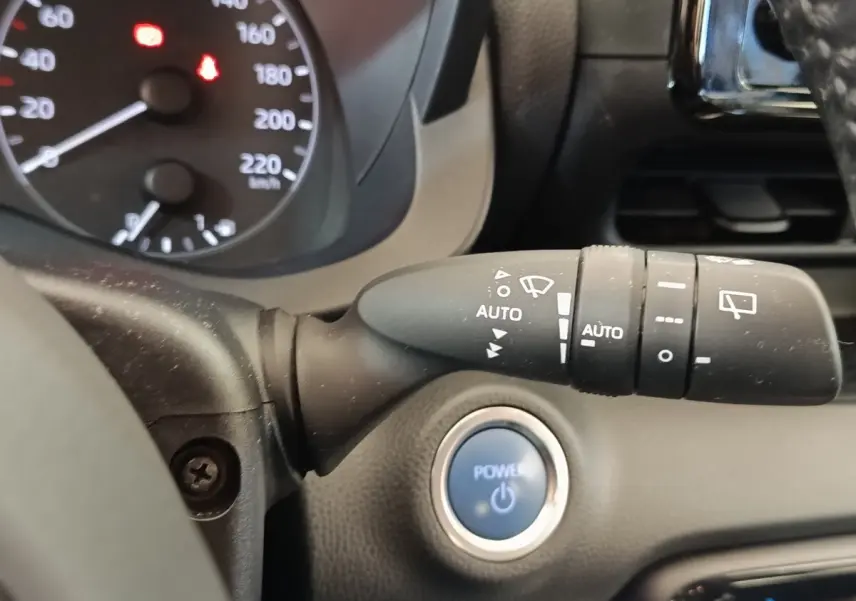 Gros plan sur la commande d’essuie-glace et le bouton start/stop bleu dans l’habitacle d’une Toyota Yaris gris clair.