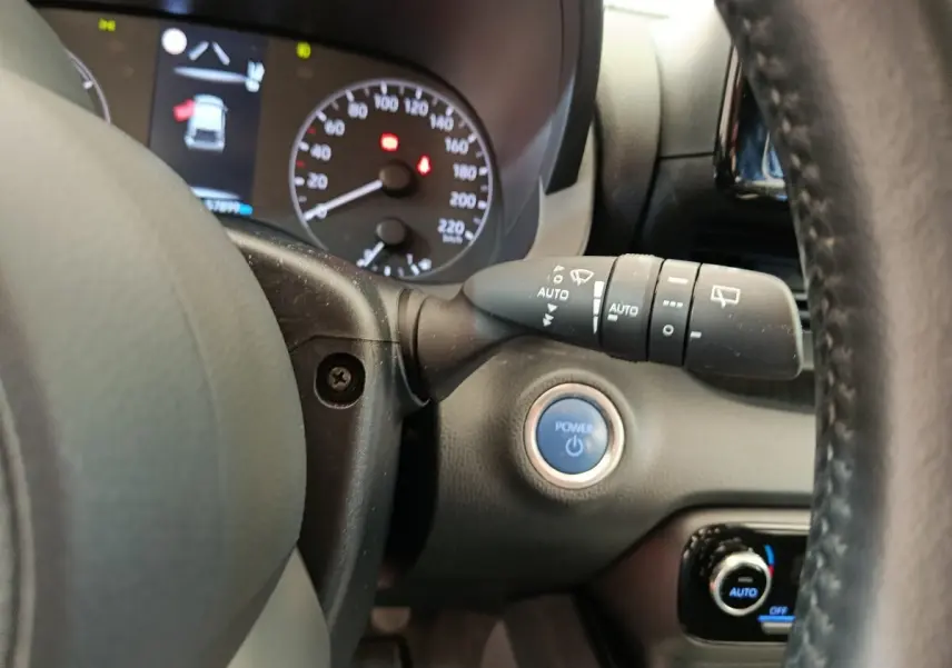 Vue rapprochée du tableau de bord de la Toyota Yaris hybride, avec bouton Power bleu et commandes au volant cuir noir.