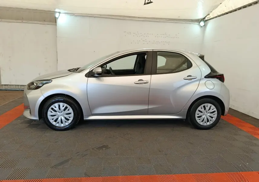 Profil droit d'une Toyota Yaris hybride gris clair 2022, avec jantes en plastique et hayon compact en arrière.