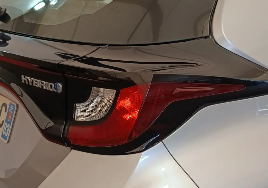 Gros plan sur le feu arrière droit gris clair d'une Toyota Yaris hybride avec logo Hybrid visible sur le coffre.