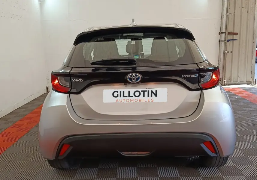 Vue arrière d'une Toyota Yaris hybride gris clair avec toit noir et feux arrière allumés dans un garage.