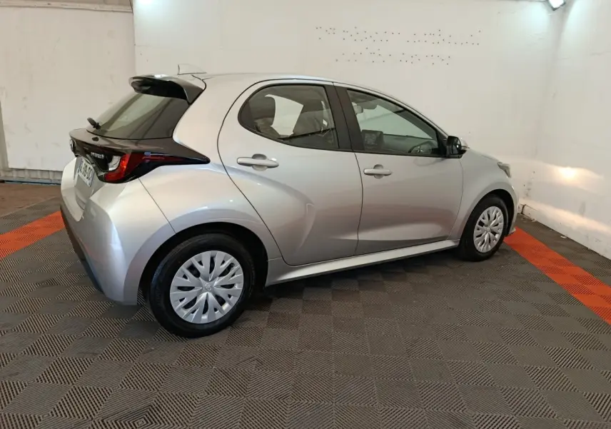 Toyota Yaris hybride gris clair vue 3/4 arrière droit, avec toit noir et jantes standard en plastique.