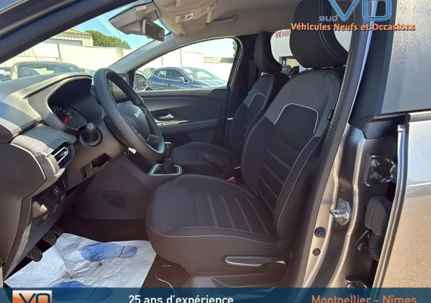 Vue intérieure côté conducteur du Dacia Jogger gris 2025, montrant les sièges avant et le volant avec levier de vitesses manuel.