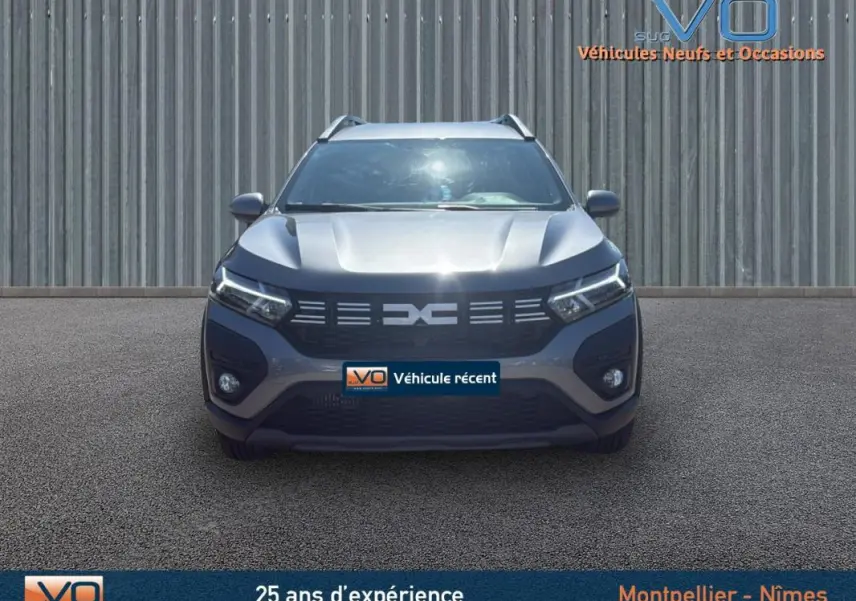 Vue frontale d'un Dacia Jogger gris 2025 avec barres de toit et feux diurnes LED allumés.