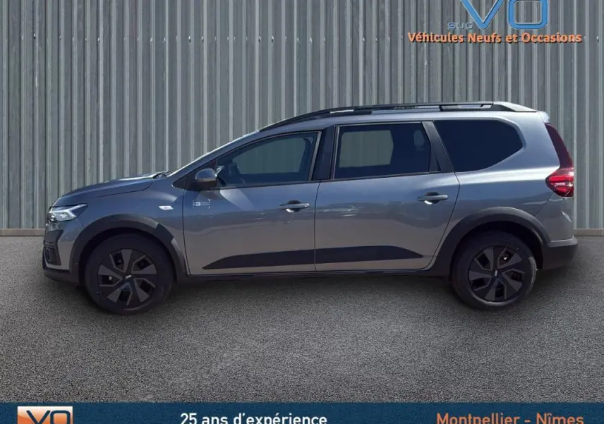 Profil latéral droit d'un Dacia Jogger gris 2025 avec barres de toit et jantes noires distinctives.