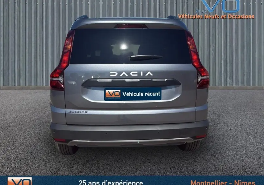 Vue arrière d'un Dacia Jogger gris 2025 avec feux verticaux et logo bien visibles sur fond urbain.