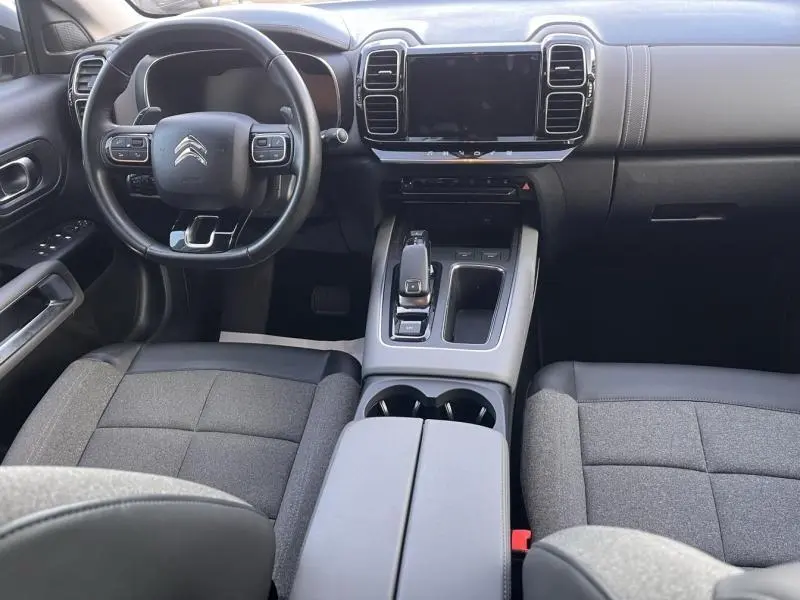 Vue intérieure avant du Citroën C5 Aircross 2021, tableau de bord noir avec volant multifonction et sièges tissu gris.