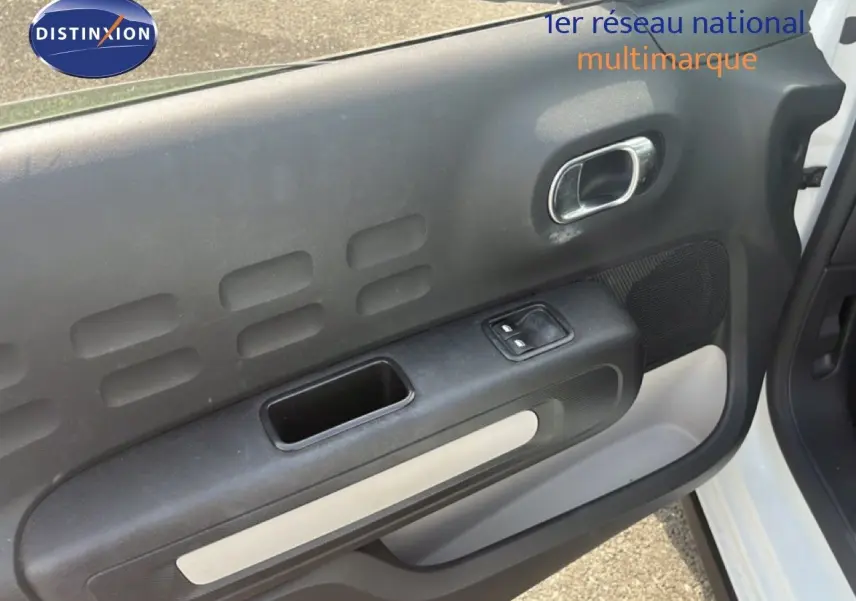Vue rapprochée de la porte avant droite blanche d'une Citroën C3 2018 avec poignée intérieure chromée et commande de vitre.