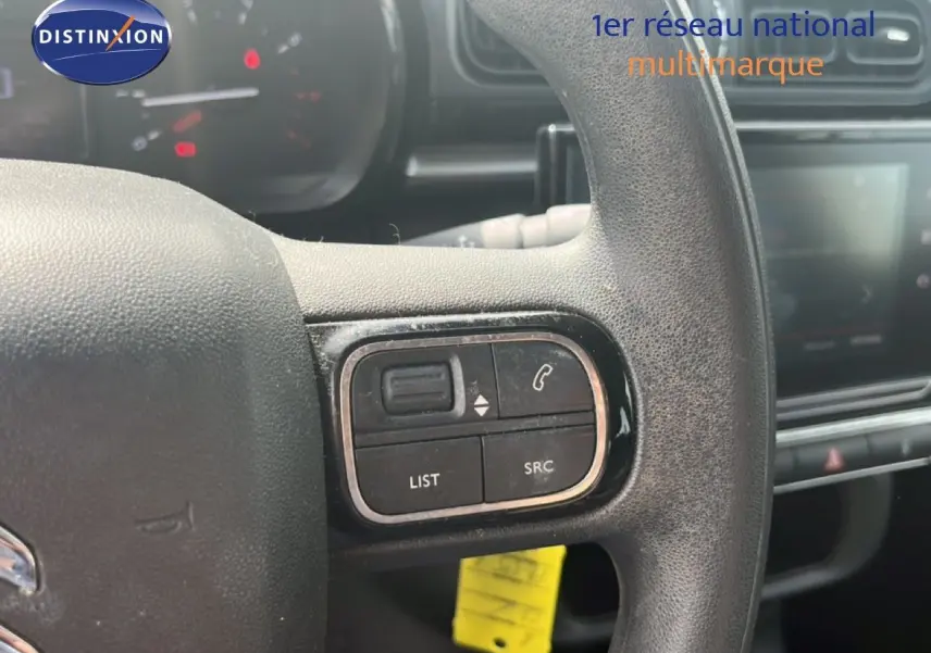 Gros plan sur les commandes au volant noir d'une Citroën C3 blanche, avec tableau de bord et écran tactile en arrière-plan.