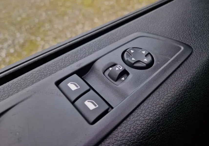 Gros plan sur les commandes de réglage des rétroviseurs et vitres côté conducteur du Citroën Jumpy Gris Titane, intérieur noir.
