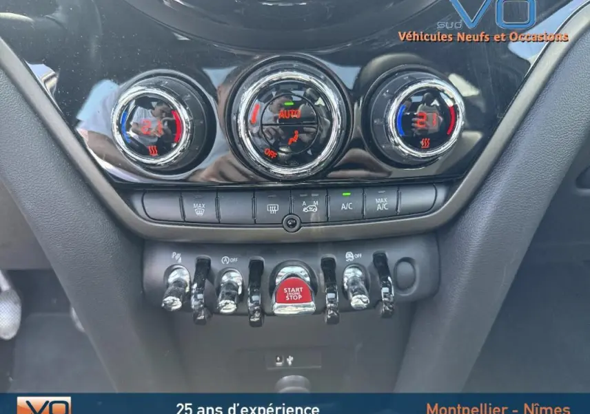 Gros plan sur la console centrale de la MINI Countryman gris clair, avec commandes de climatisation et bouton start/stop rouge.