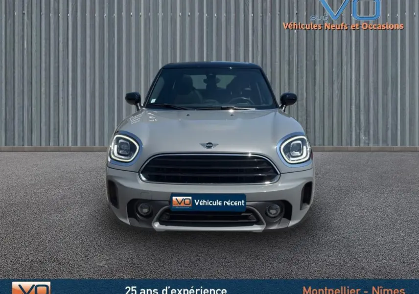 Vue frontale d'une MINI Countryman gris clair avec phares LED allumés et calandre noire, sur fond industriel.