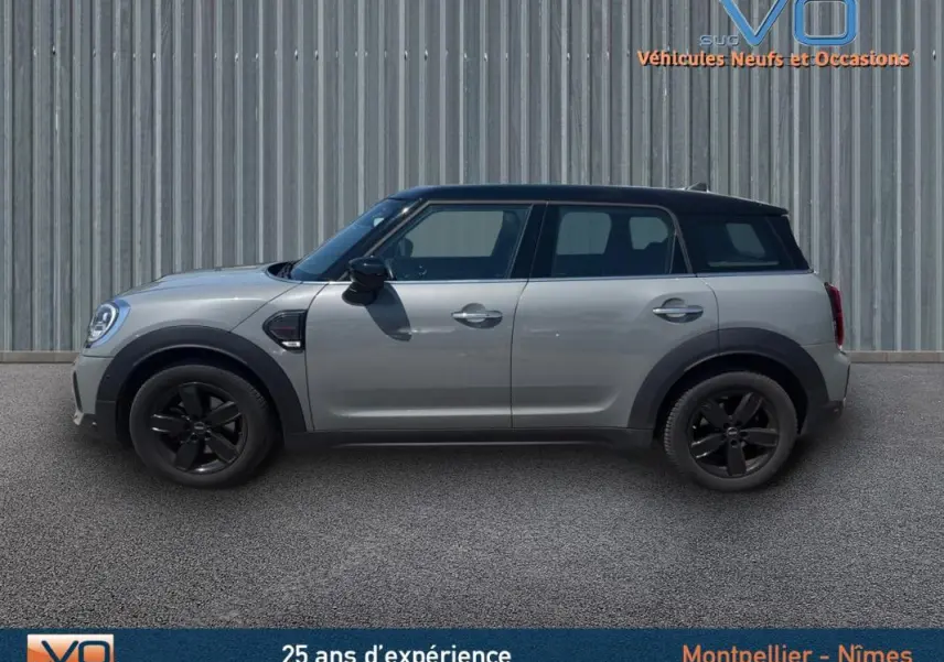 Profil côté gauche d'une MINI Countryman gris clair avec toit noir et jantes alliage noires sur fond urbain.
